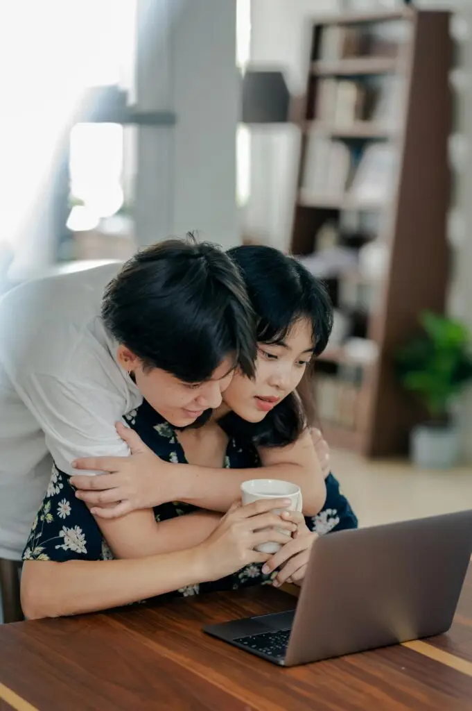 A couple shares a loving moment while working on a laptop indoors.